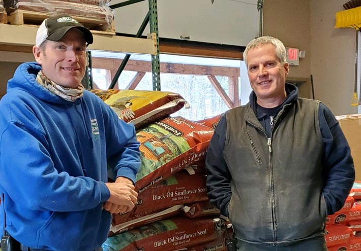 Brothers Tom and Paul Osborne smiling and standing by a pallet of stacked seed bags 